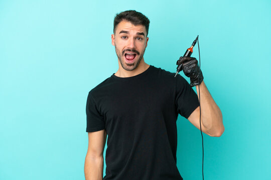 Young tattoo artist man isolated on blue background with surprise facial expression