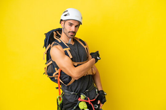 Young caucasian rock climber man isolated on yellow background pointing back