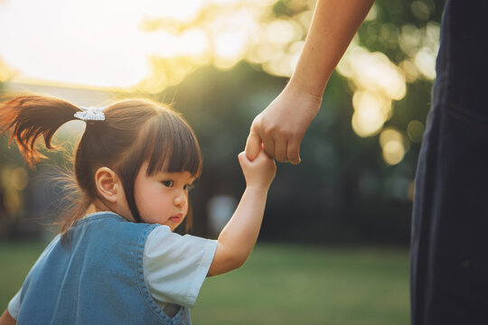 Mother holding toddler daughter's hand while walking together outdoors at sunset, showing parental care, guidance, protection, trust, family bonding, childhood support and loving motherhood