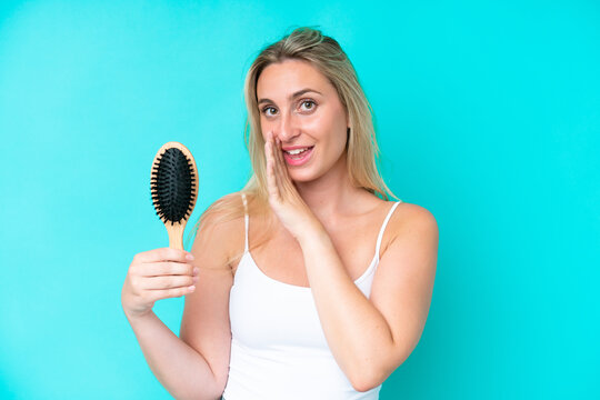 Young caucasian woman with hair comb isolated on blue background whispering something