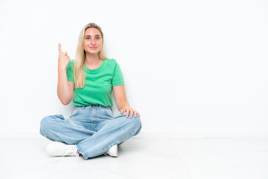 Young caucasian woman sitting on the floor isolated on white background pointing with the index finger a great idea