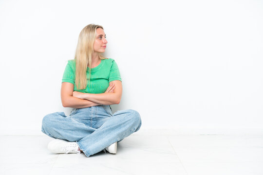 Young caucasian woman sitting on the floor isolated on white background in lateral position