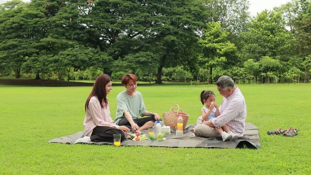 Happy mother and daughter, Happy Asian family having fun time on picnic at city nature park sunny day, outdoor activitie with daughter father, mother and grandfather
