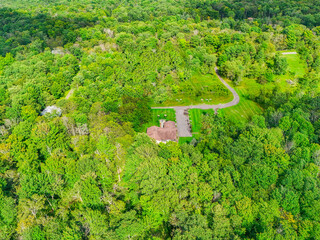 High aerial view of a small house nestled in a clearing within a dense green forest with secluded home woodland cabin residential property rural home countryside living house in woods © SMHT ART WORKS