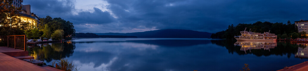 Obraz premium Panoramic view of Lake Akan at blue hour in Akankohan, Hokkaido, Japan, with mountains, lakeside buildings, boats, and reflections on the water.