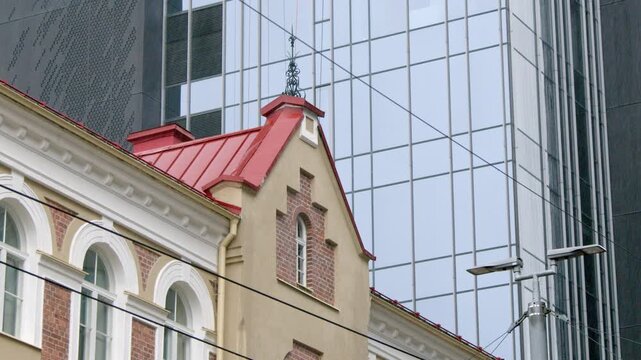 Historic brick building with red metal roof contrasted against modern glass architecture in Tallinn, Estonia, with visible summer rain falling in slow motion over the urban cityscape.