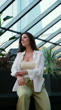 Relaxed woman in casual clothes rolling up her sleeves while waiting on a bench