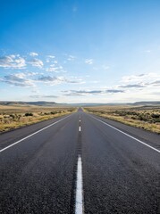 Fototapeta premium Endless open road stretching towards the horizon under a vast blue sky.