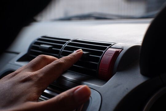 Person hand adjusting airflow direction louvers on car air conditioner vent grille on vehicle dashboard.