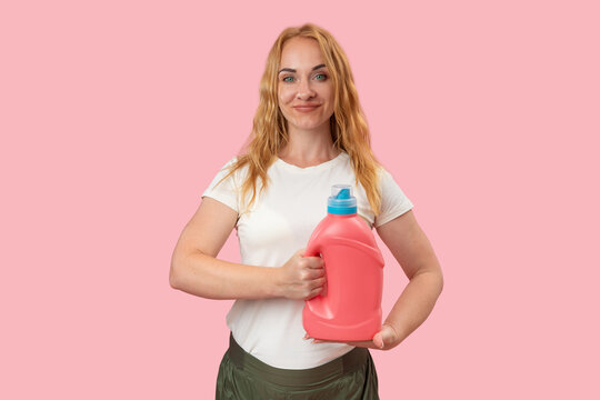 Smiling woman holding a pink plastic bottle of liquid laundry detergent or fabric softener against a light pink background, representing daily household chores and cleaning products