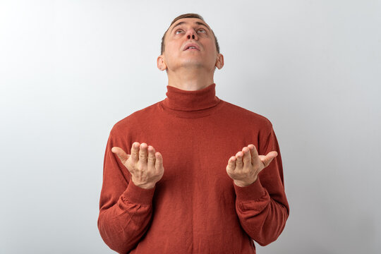 Man with open palms looking upward in a white studio, expressing hope, prayer and seeking guidance, a contemplative gesture of faith, request or expecting help