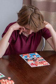 Teenage boy concentrating over a card game with red markers on a table at home, displaying focused thought and slight frustration during leisure play and strategy practice