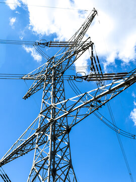Power line tower under blue sky. A metal power line tower stands tall against the bright blue sky. Wires stretch across the structure under sunlight.