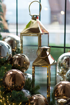 Elegant lanterns and metallic Christmas ornaments with glowing lights and evergreen branches by a bright window, luxurious festive holiday decoration, cozy winter celebration atmosphere