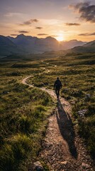 Fototapeta premium Lone Hiker Walks on Winding Path Through Grassy Valley Towards Mountain Sunset.