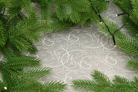 Christmas evergreen branches with glowing string lights on an elegant silver ornamental background, festive winter decoration with copy space, cozy holiday atmosphere, New Year celebration design