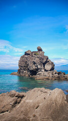 Obraz premium Vertical rock column formation called sea stack extending out of the water under a vivid blue sky. Apo Island, Philippines