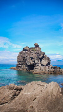 Vertical rock column formation called sea stack extending out of the water under a vivid blue sky. Apo Island, Philippines