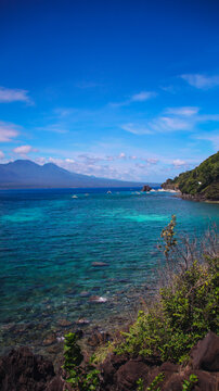 Coastal wide view of blue sea waters, rocky shores, lush greenery and distant mountains under a cloudy sky in Apo Island. Dauin, Philippines
