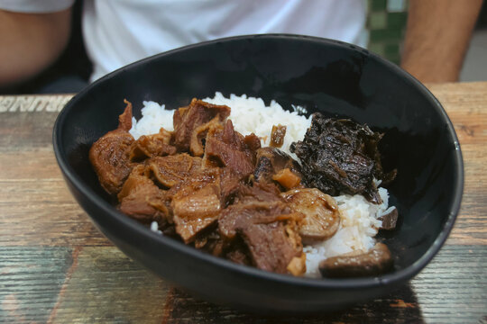 Braised beef (Ngau Lam) with chu hou paste, fermented spinach and rice in a black bowl, traditional local Cantonese dish served in street side food stall called dai pai dong. Central, Hong Kong