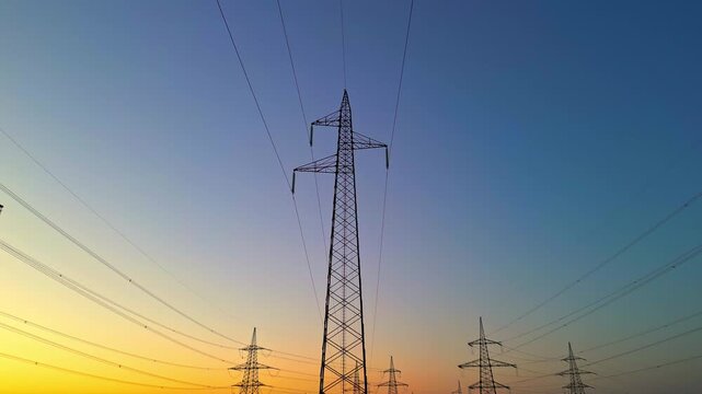 Power lines stand tall against a vibrant sunset symbolizing reliable power essential for modern living. Skilled maintenance engineers ensure uninterrupted electricity flow.