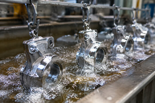 Metal parts bubbling in an electroplating tank, silver coating covering surfaces in an industrial detail shot.