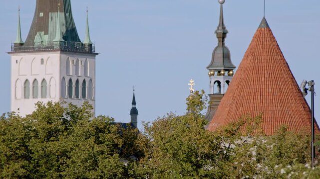 Static 4K footage of historic towers and church architecture in Tallinn Old Town, Estonia, featuring St. Olaf&rsquo;s Church tower and red tiled medieval rooftops surrounded by green summer trees.