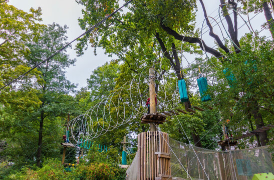 Suspended rope course with turquoise climbing elements and circular wire obstacles among dense green trees at an outdoor adventure park, aerial recreational structure