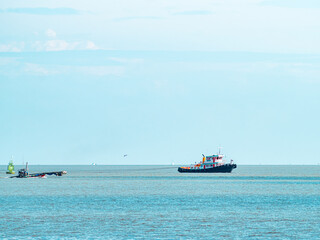 Colorful tugboat towing a small fishing boat with rope across calm blue sea, green navigation buoy and seagull on horizon, minimal seascape with copy space © Tavan