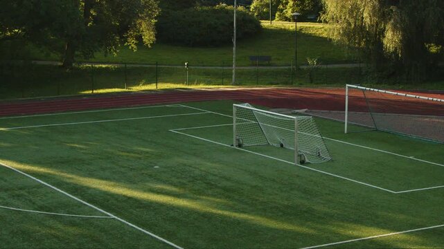 Locked off 4K footage of an empty outdoor football field with full size and portable soccer goals, surrounded by running track and green park in Tallinn, Estonia, illuminated by warm evening sunlight