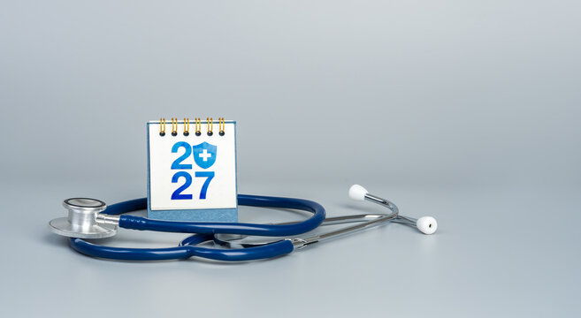 Stethoscope surrounds new year 2027 desk calendar with medical shield symbol. Health insurance, health check-up, healthcare planning, patient protection, annual strategy, and medical coverage.
