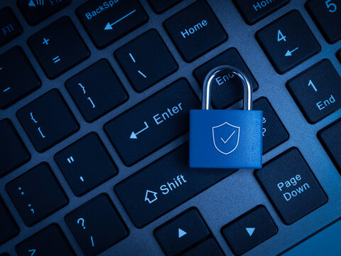 Blue padlock with shield symbol rests on computer keyboard background. Secure digital access, data protection, authentication, privacy, account safety, and cybersecurity risk prevention concept.