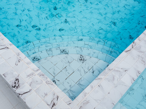 Tiled swimming pool steps seen through clear blue water with marble-pattern edges, representing aquatic facility design, pool construction, renovation, maintenance, safety, and resort recreation.