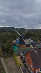 Outwood Windmill, Outwood, Surrey, United Kingdom: Aerial view of the historic 17th-century black smock and post mill with white sails and traditional rural surroundings on a cloudy day. © Serhii