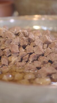 Slow motion close up of diced beef chunks sizzling in hot oil in a metal pan