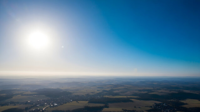 Panoramic aerial view of a vast countryside landscape under a bright sunlit blue sky with a clear horizon line at dawn