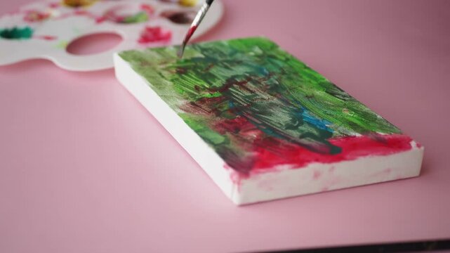 Artist paints abstract art on canvas with green and red colors using brush, close up shot