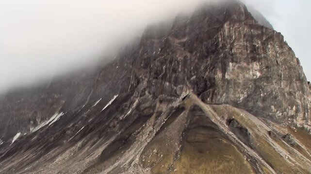 A steep rocky mountain peak rises into fog above the cold coast. The image retains a sloping ridge and close framing as secondary detail, while light and texture shape the wider scene.