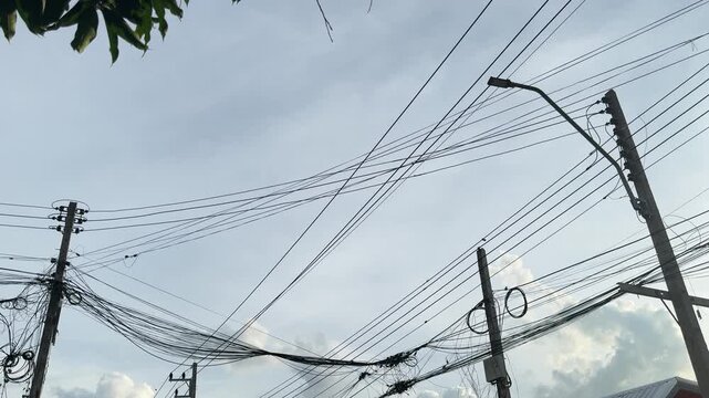 Chaotic messy electric wires and cables on poles against sky background