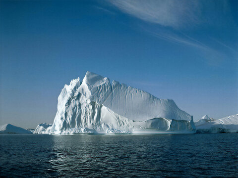 Massive white iceberg floating in blue polar ocean under clear sky