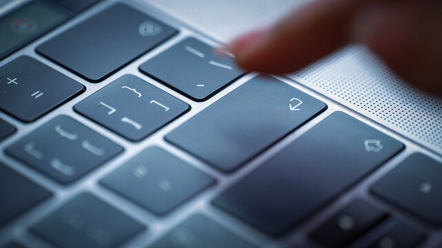 Finger pressing enter key on laptop keyboard close-up