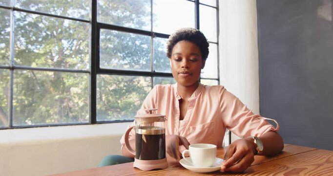 African American woman enjoying coffee at office desk near large window