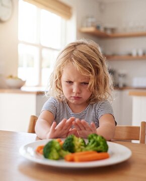 Frustrated toddler at the kitchen table with plate of vegetables
