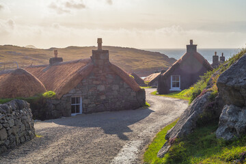 Gearrannan Blackhouse Village with thatched stone cottages, heather and coastal bay at golden hour, Isle of Lewis, Outer Hebrides, Scotland © EyesTravelling