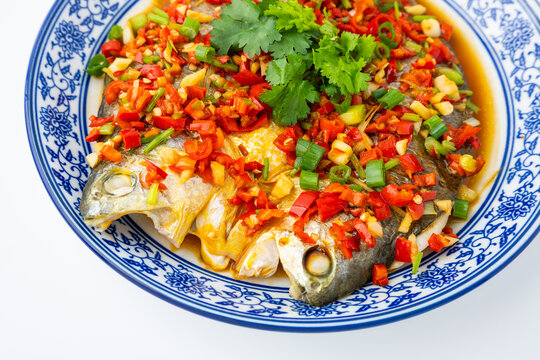 A plate of Hunan-style steamed yellow croaker with chopped chili peppers, set against a white background.