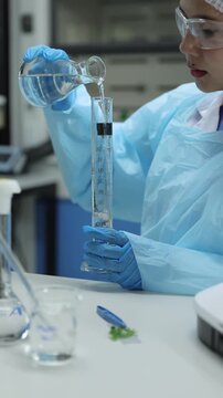 Female scientist pouring liquid into a graduated cylinder.