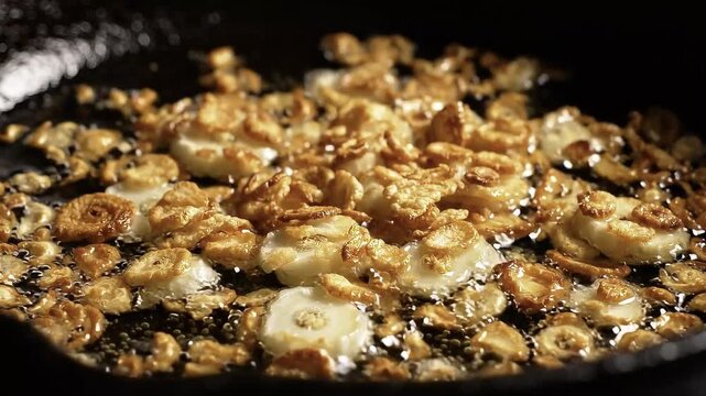 Sizzling garlic slices frying in hot oil, crispy golden garlic chips cooking in a black cast iron skillet, close-up food preparation 4K Video