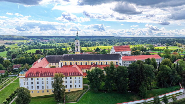 Malerische Luftaufnahme von Ochsenhausen mit der barocken Klosteranlage, eingebettet in die idyllische, gr&uuml;ne H&uuml;gellandschaft Oberschwabens unter blauem Sommerhimmel mit Wolken.