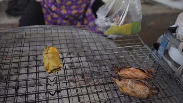 Traditional Thai coconut pancake Ba Bin cooking on banana leaf over charcoal grill, authentic street food dessert, stock footage video.