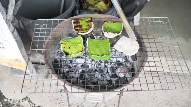 Traditional Thai coconut pancake Ba Bin cooking on banana leaf over charcoal grill, authentic street food dessert, stock footage video.